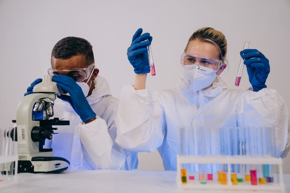 Two scientists in protective gear working with microscope and test tubes in a lab.